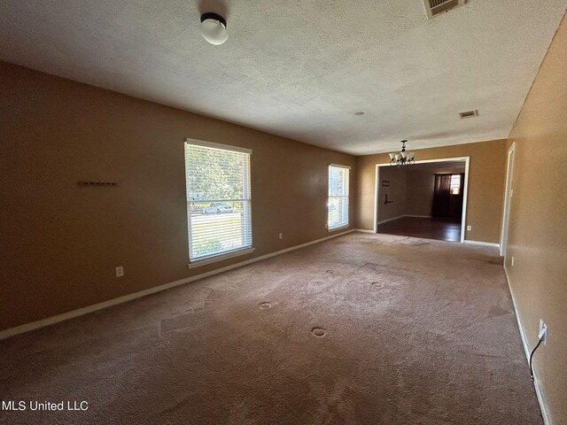 carpeted spare room with a textured ceiling and a chandelier