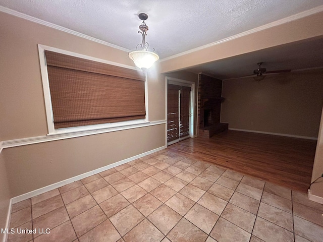 empty room with a textured ceiling, a brick fireplace, ceiling fan, hardwood / wood-style flooring, and ornamental molding