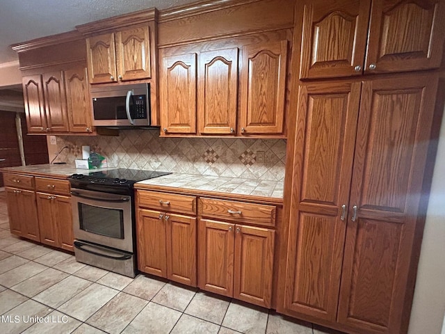 kitchen featuring decorative backsplash, light tile patterned flooring, stainless steel appliances, and tile counters