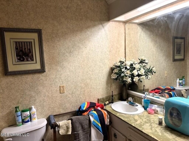 bathroom with toilet, wallpapered walls, and vanity