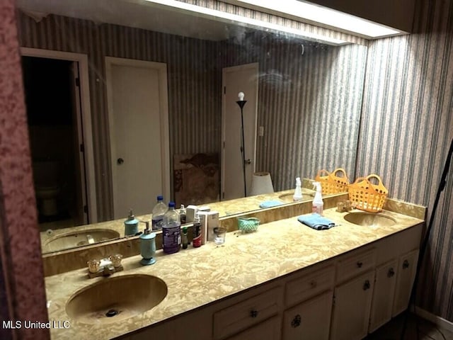 full bathroom featuring double vanity, a sink, and wallpapered walls