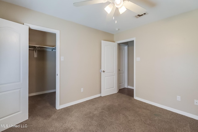 unfurnished bedroom featuring ceiling fan, a closet, a walk in closet, and dark colored carpet