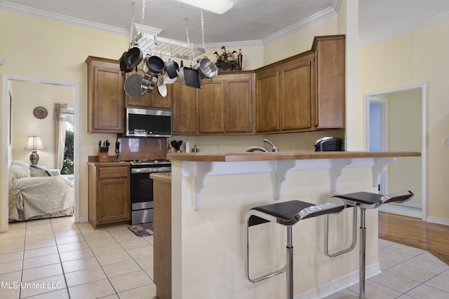 311 Pinecrest Blvd, Long Beach, MS 39560 - kitchen with stainless steel appliances, a kitchen bar, light tile patterned floors, brown cabinetry, and tasteful backsplash