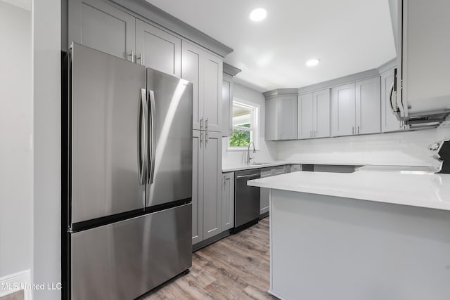 kitchen featuring gray cabinetry, sink, stainless steel appliances, tasteful backsplash, and light wood-type flooring