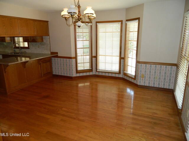 unfurnished dining area with a notable chandelier, sink, and light wood-type flooring