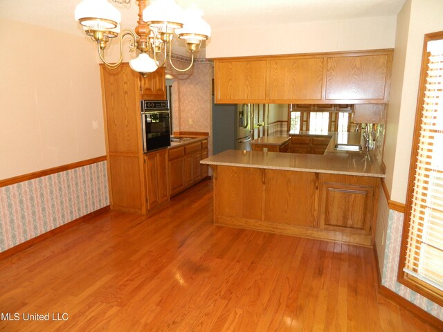 kitchen featuring a notable chandelier, light hardwood / wood-style floors, kitchen peninsula, and black oven