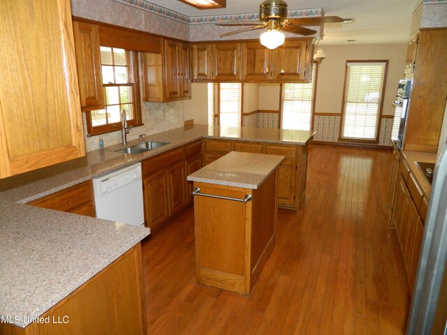 kitchen with kitchen peninsula, wood-type flooring, dishwasher, sink, and a center island