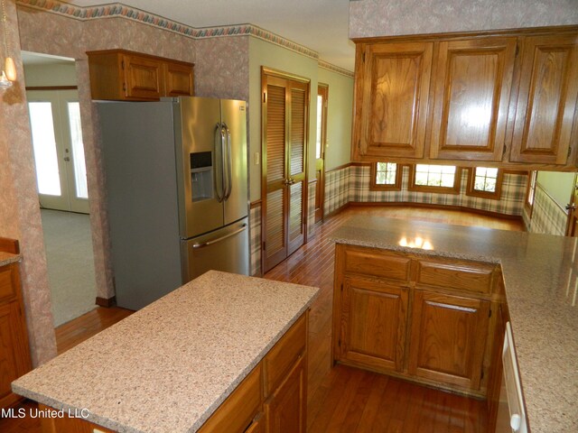 kitchen featuring light stone counters, a kitchen island, stainless steel refrigerator with ice dispenser, and wood-type flooring