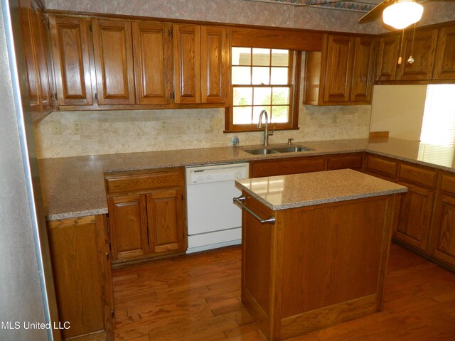 kitchen with a kitchen island, hardwood / wood-style flooring, white dishwasher, sink, and light stone countertops