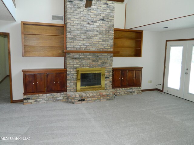 unfurnished living room with french doors, a brick fireplace, and light colored carpet