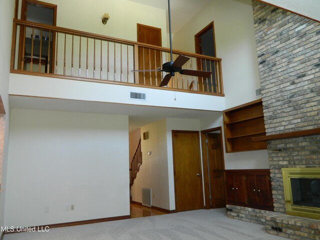 unfurnished living room with ceiling fan, a high ceiling, a fireplace, and carpet floors