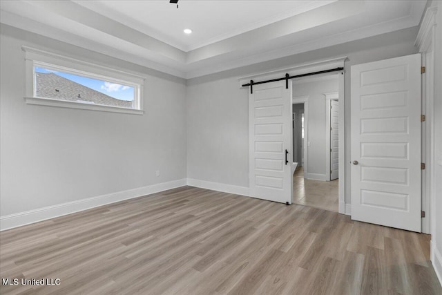 unfurnished bedroom featuring ornamental molding, a barn door, and light hardwood / wood-style flooring