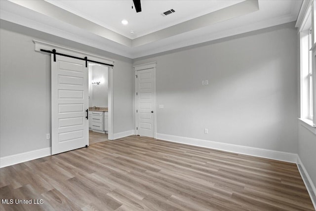 unfurnished bedroom featuring ensuite bath, ornamental molding, light wood-type flooring, and a barn door