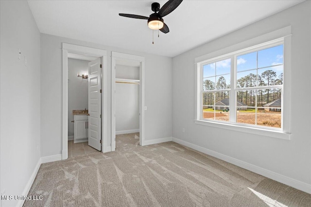 unfurnished bedroom featuring connected bathroom, ceiling fan, multiple windows, and light colored carpet