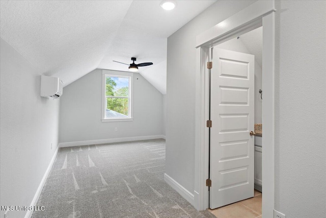 additional living space with a wall mounted air conditioner, a textured ceiling, ceiling fan, vaulted ceiling, and light colored carpet