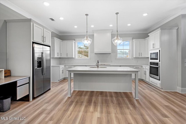 kitchen with appliances with stainless steel finishes, light hardwood / wood-style flooring, decorative light fixtures, and crown molding