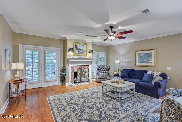 living room with ceiling fan, visible vents, crown molding, a brick fireplace, and wood finished floors