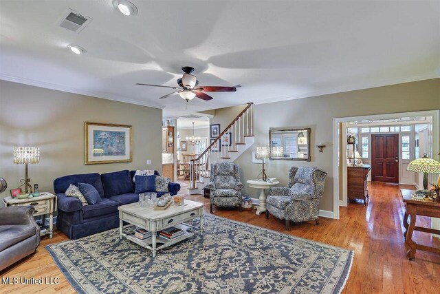 living area featuring visible vents, crown molding, ceiling fan with notable chandelier, and wood finished floors