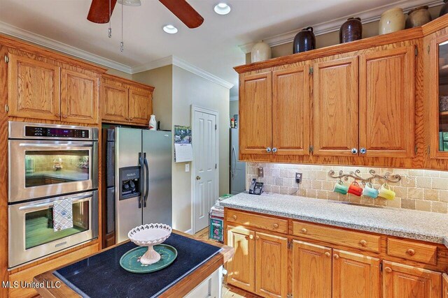 kitchen featuring ceiling fan, brown cabinetry, backsplash, ornamental molding, and stainless steel appliances