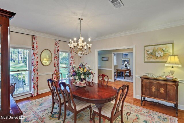 dining room featuring an inviting chandelier, ornamental molding, wood finished floors, and visible vents