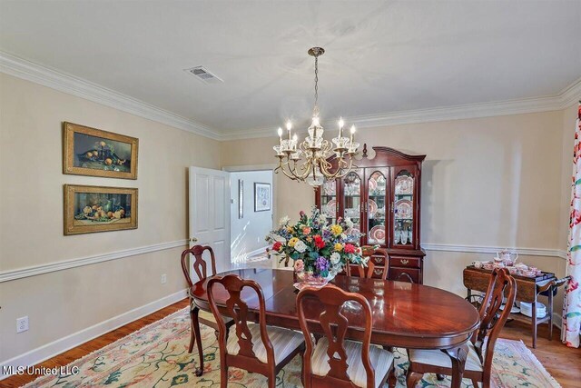 dining room with visible vents, ornamental molding, wood finished floors, baseboards, and a chandelier