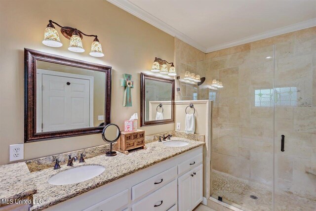 bathroom with a sink, ornamental molding, a shower stall, and double vanity
