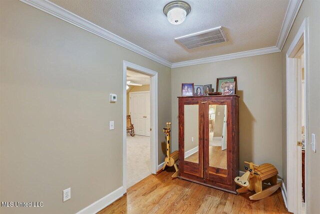 interior space with a textured ceiling, ornamental molding, wood finished floors, and visible vents