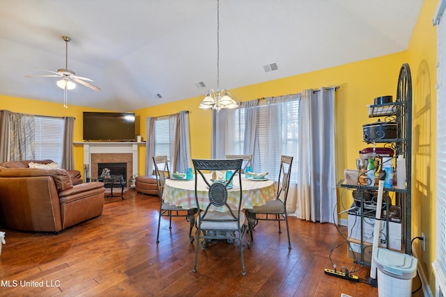 dining room featuring hardwood / wood-style floors, a fireplace, ceiling fan with notable chandelier, and vaulted ceiling