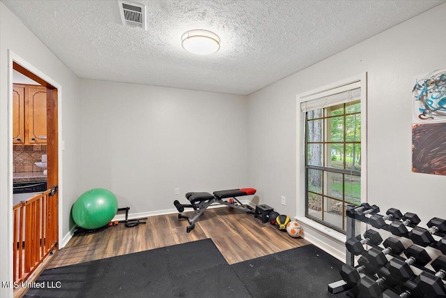 exercise room featuring a textured ceiling, visible vents, wood finished floors, and baseboards