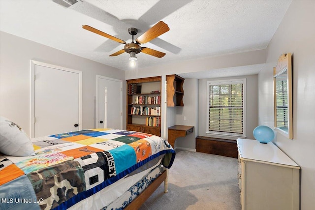 bedroom with a textured ceiling, visible vents, a ceiling fan, and light colored carpet
