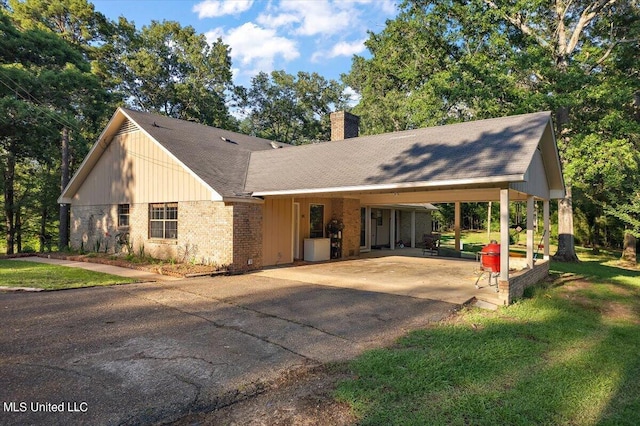 view of front of house featuring a front lawn, a chimney, a carport, brick siding, and concrete driveway