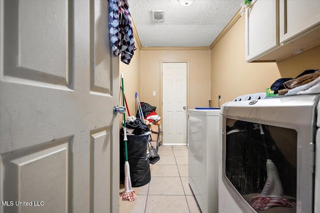 laundry room with light tile patterned flooring, cabinets, a textured ceiling, ornamental molding, and washing machine and dryer