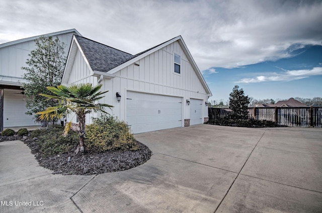 view of home's exterior featuring a garage, a shingled roof, concrete driveway, fence, and board and batten siding