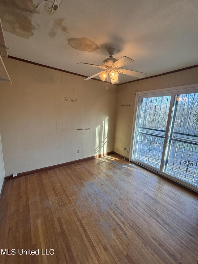 empty room with ornamental molding, ceiling fan, baseboards, and wood finished floors