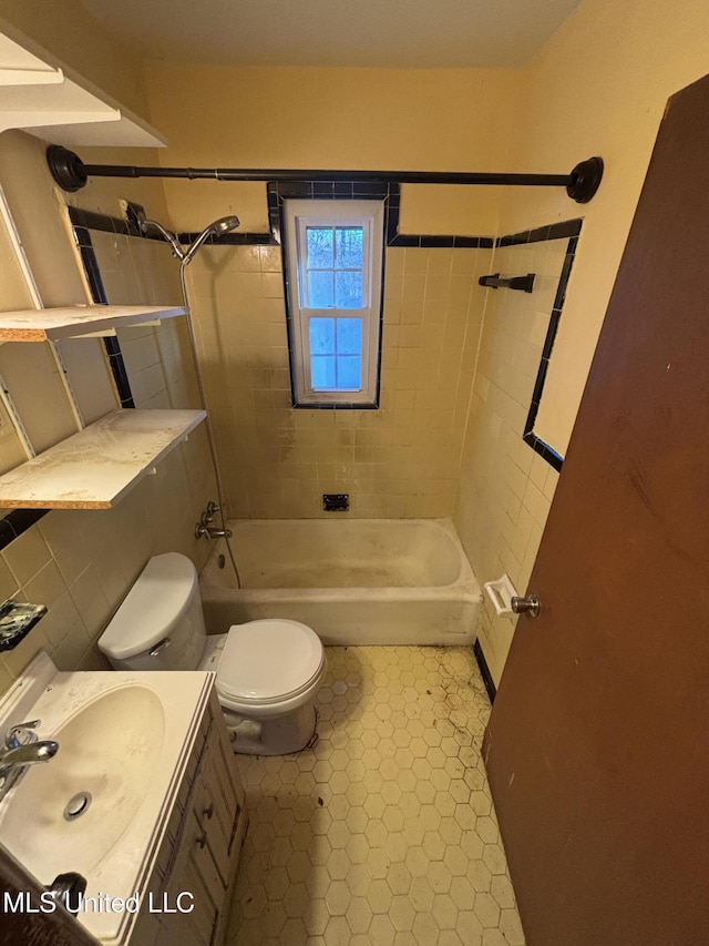 full bath with toilet, tile patterned floors, vanity, washtub / shower combination, and tile walls