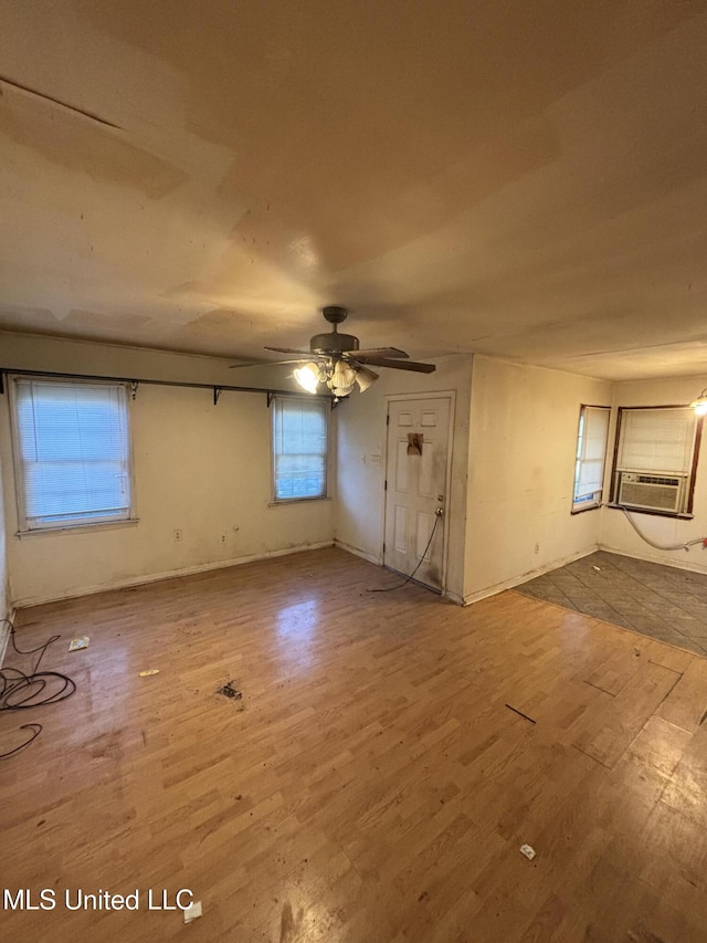 interior space with a ceiling fan, baseboards, cooling unit, and wood finished floors