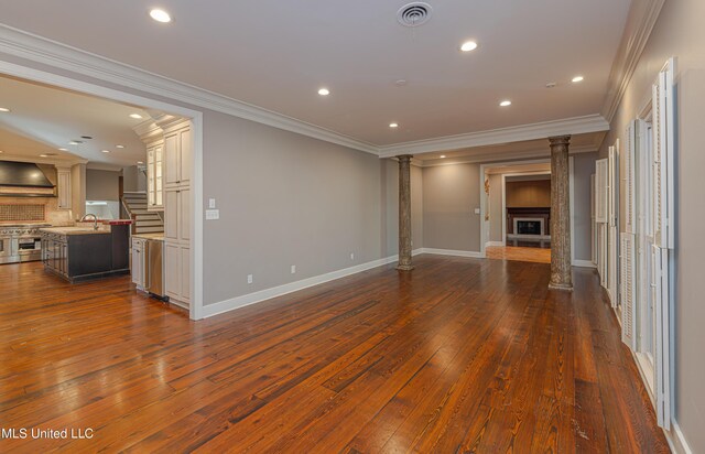 unfurnished living room featuring a sink, visible vents, baseboards, decorative columns, and crown molding