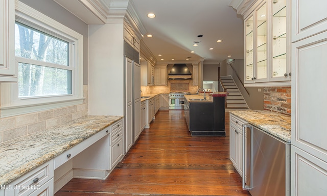 kitchen featuring wall chimney exhaust hood, glass insert cabinets, range with two ovens, and built in study area