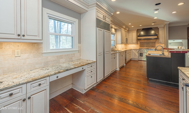 kitchen featuring dark wood finished floors, built in desk, stainless steel stove, a sink, and premium range hood