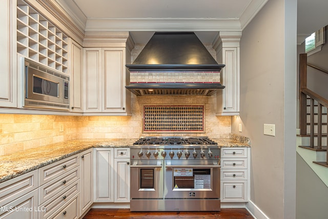 kitchen with tasteful backsplash, light stone counters, cream cabinets, custom exhaust hood, and stainless steel appliances