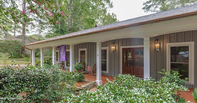 doorway to property featuring board and batten siding, covered porch, and french doors