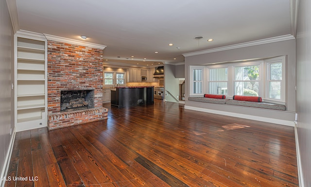 unfurnished living room featuring baseboards, ornamental molding, dark wood-type flooring, a brick fireplace, and recessed lighting