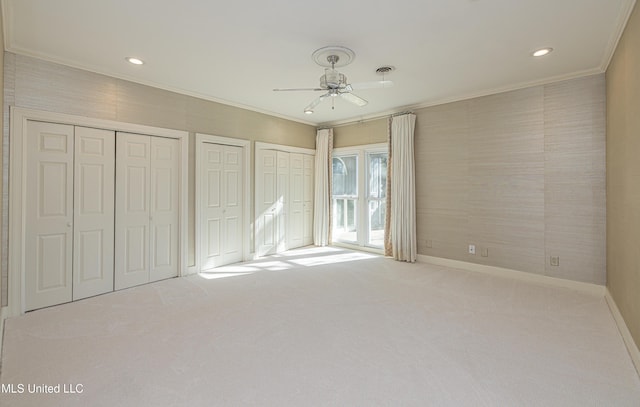 unfurnished bedroom featuring multiple closets, ornamental molding, carpet flooring, ceiling fan, and baseboards