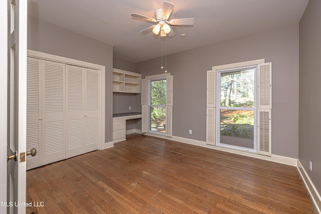 unfurnished bedroom with multiple windows, baseboards, dark wood-style flooring, and built in study area