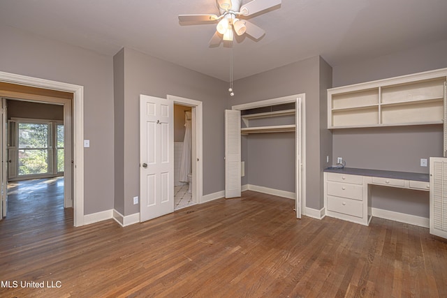 unfurnished bedroom featuring baseboards, built in study area, ceiling fan, dark wood-type flooring, and a closet