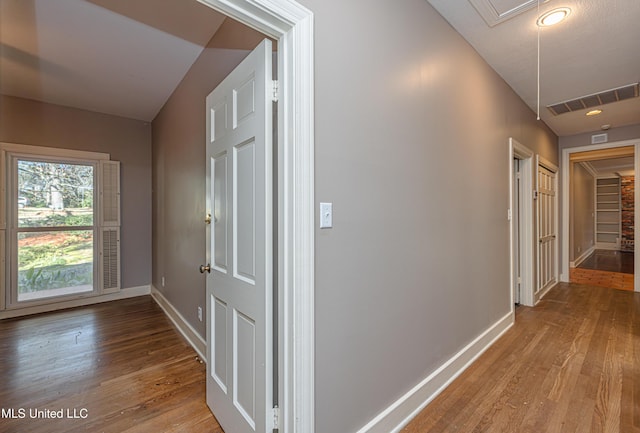 hallway featuring baseboards, light wood finished floors, visible vents, and attic access