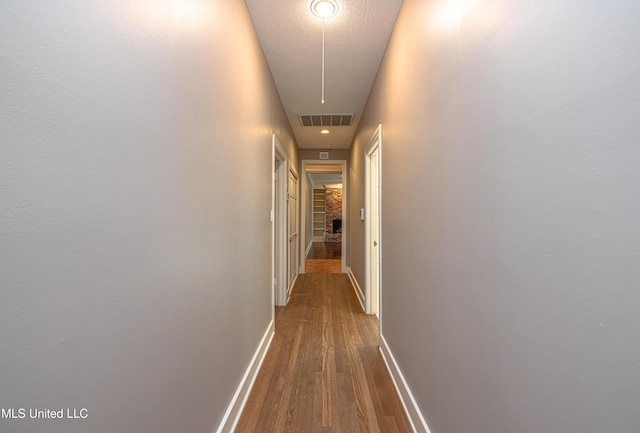 corridor with dark wood-style flooring, visible vents, a textured ceiling, and baseboards