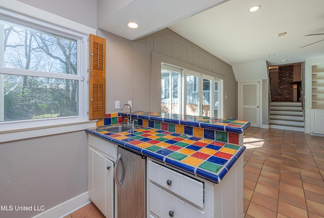 kitchen featuring light tile patterned floors, tile counters, white cabinetry, a sink, and a peninsula