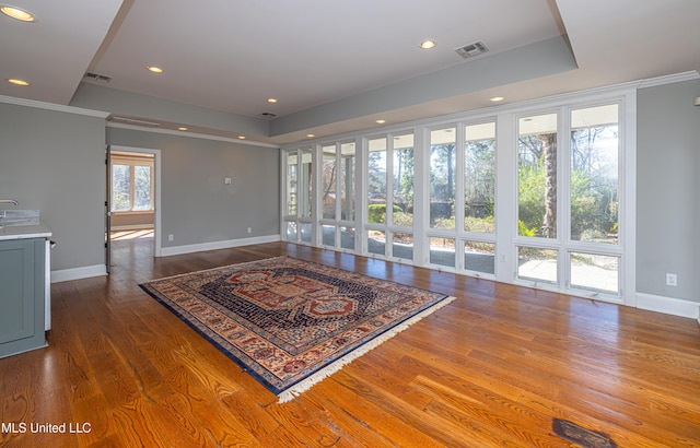 unfurnished living room featuring a raised ceiling, visible vents, baseboards, and wood finished floors