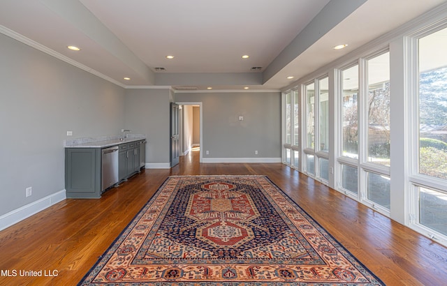 living area with recessed lighting, wood finished floors, baseboards, ornamental molding, and a tray ceiling